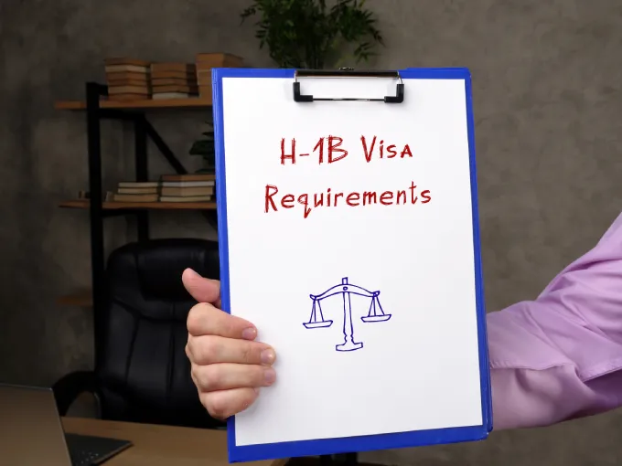 Mans arm holding a clipboard stating h-1B visa requirements