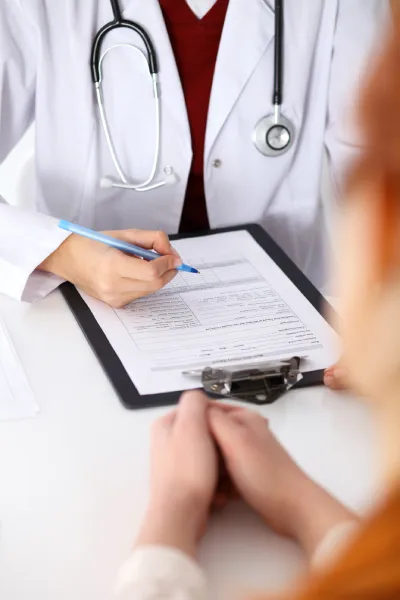 Close up of a female civil surgeon filling up a form while consulting patient